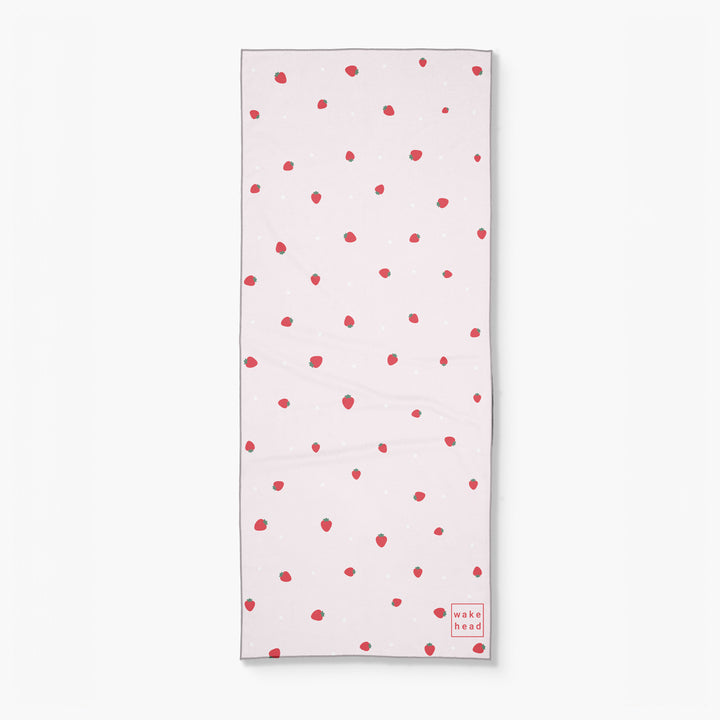 White lake towel with red strawberry pattern and "wake head" logo in red at the bottom right corner.