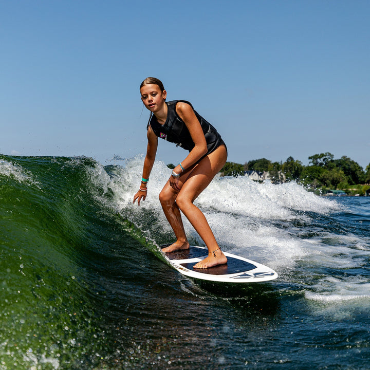A young woman surfing on a 2026 Phase Five Surfari board, riding a wave with clear blue skies in the background.