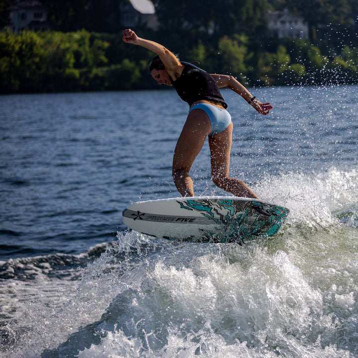 A person performing a trick on a 2026 Phase Five Swell surfboard, creating splashes on a lake.