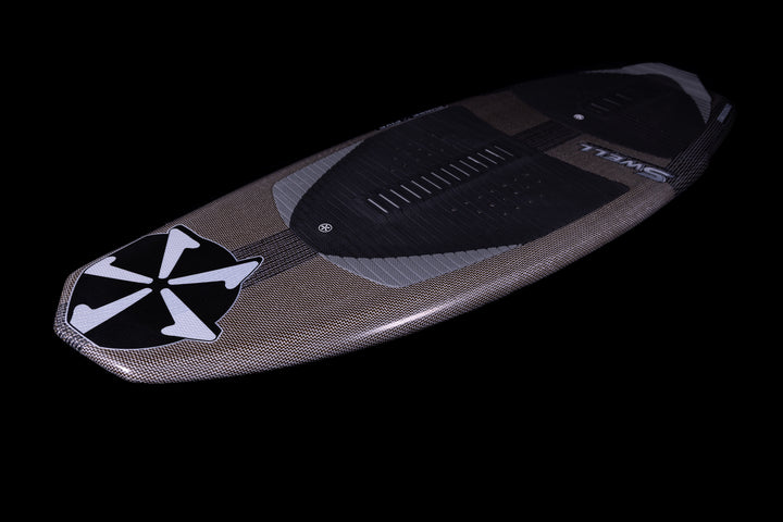 2025 Phase 5 Swell Stealth surfboard with a sleek, textured design, black traction pad, and prominent logo on a black background.