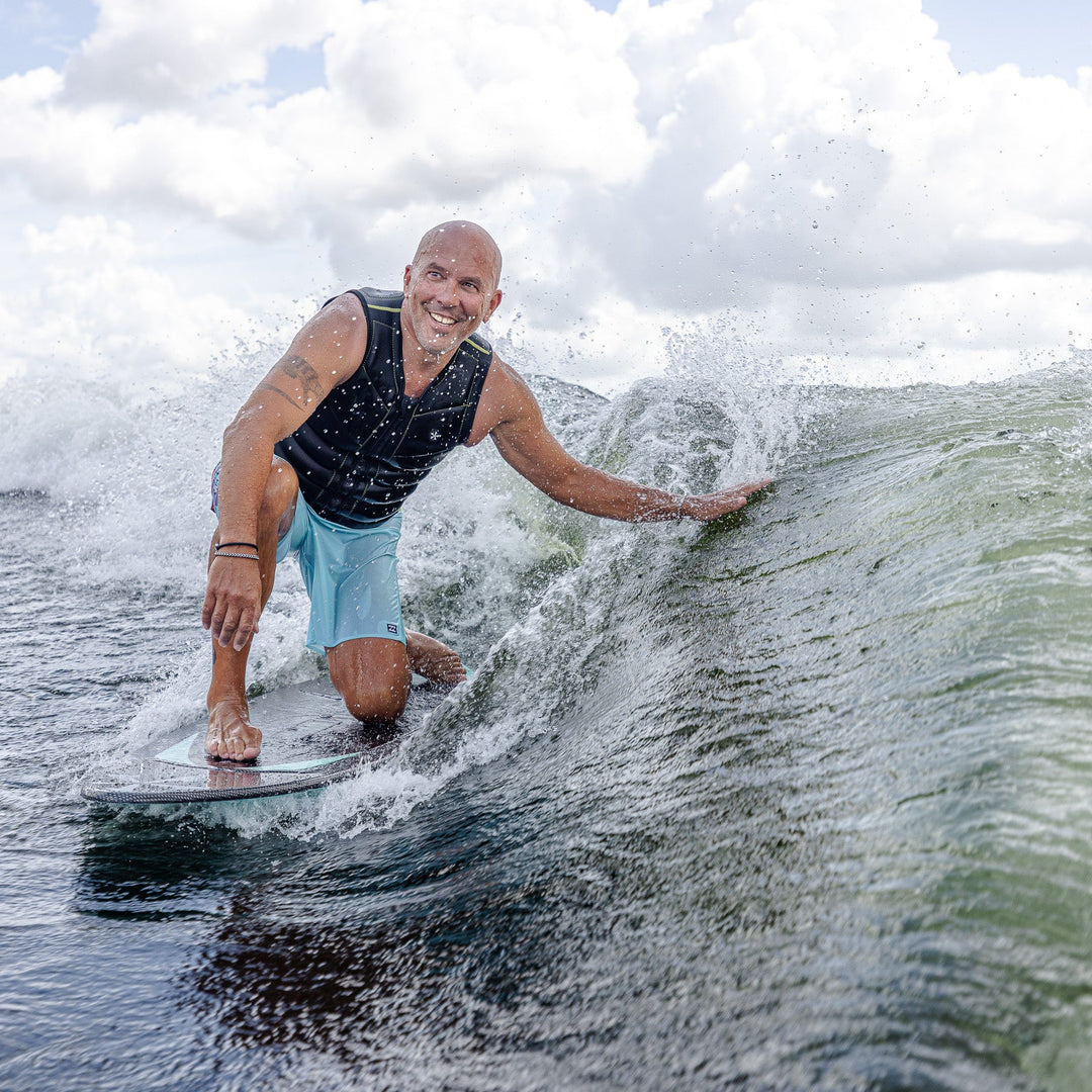 A person riding the 2026 Phase Five Trident V3 surfboard, carving through a wave with a smile on a sunny day.