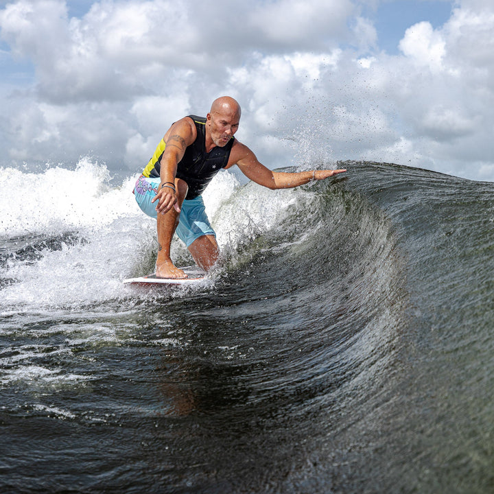 A person riding the 2026 Phase Five XB surfboard on a wave, showcasing skill and balance in a dynamic water setting.
