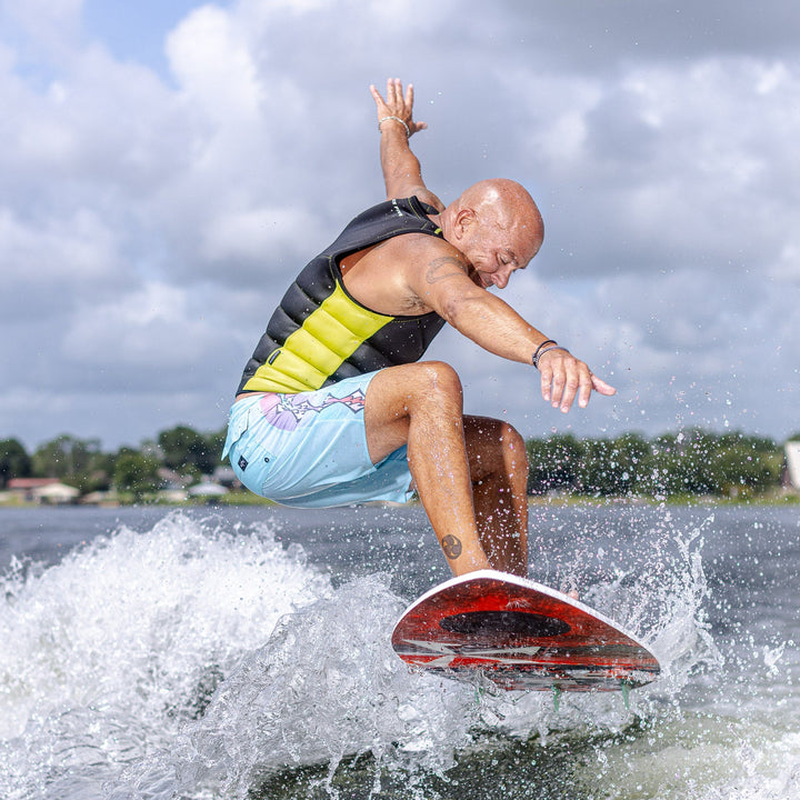 A person performs a trick on a 2026 Phase Five XB surfboard, showcasing vibrant water and a dynamic sky backdrop.