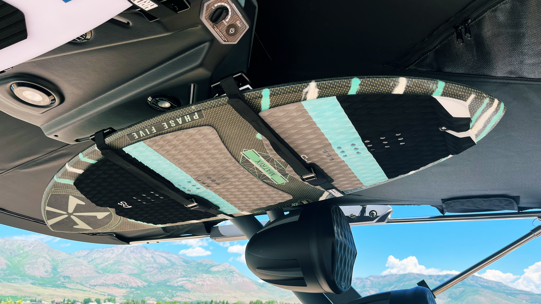 Surfboard secured on GX Towers XR1 Surf Rack inside a vehicle, with scenic mountains and blue sky in the background.
