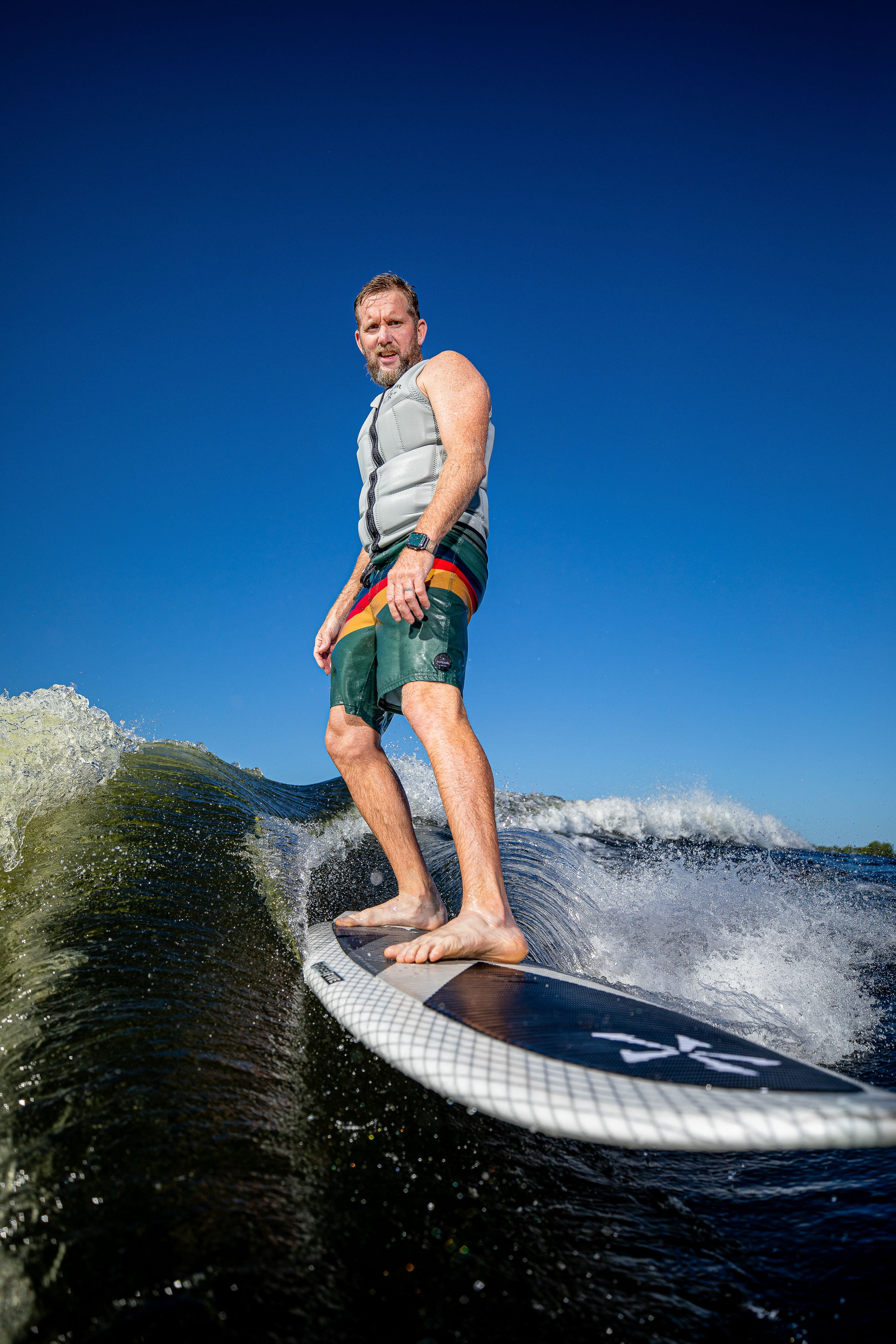 A man surfing on a 2025 Phase 5 Zilla surfboard, riding a wave with a clear blue sky in the background.
