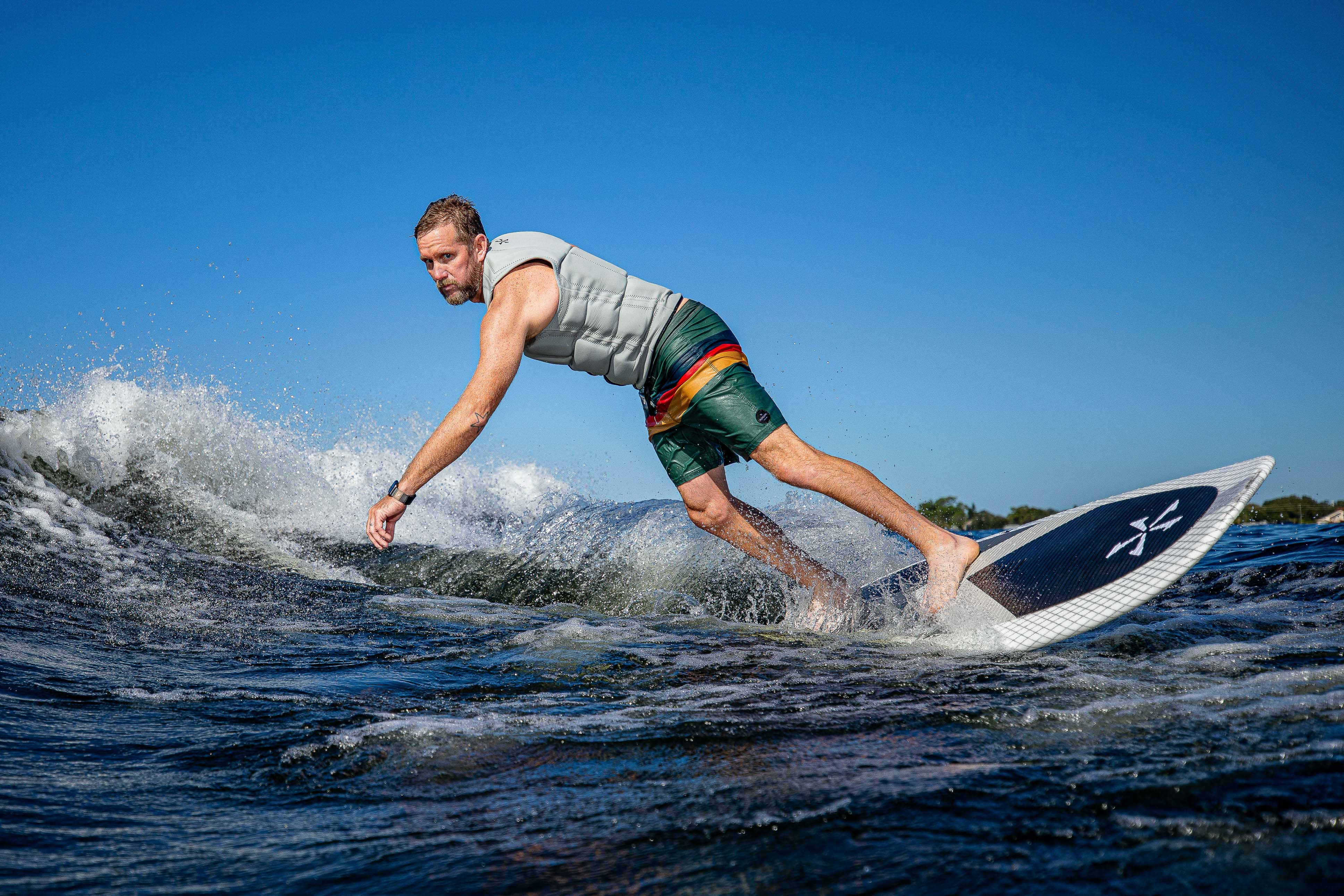 Man surfing on the 2025 Phase 5 Zilla Surf Board on a wave under clear blue skies.
