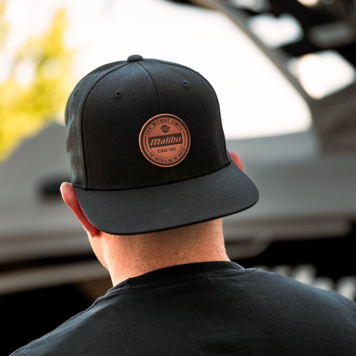 Back view of a person wearing a black "Limitless Hat" with a round patch featuring the Malibu logo and text.