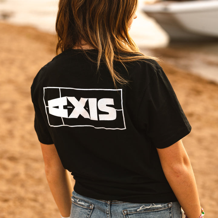Black Axis logo T-shirt with white graphic print on the back, worn by a woman at the beach.