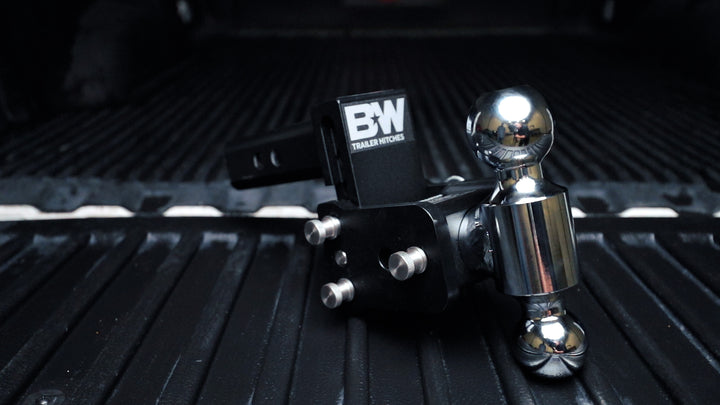 Black B&amp;W TOW &amp; STOW adjustable ball mount with chrome hitch ball, mounted on a black surface.